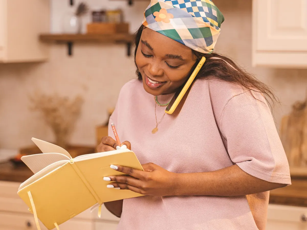 Una mujer en su cocina, al teléfono, apuntando en un cuaderno