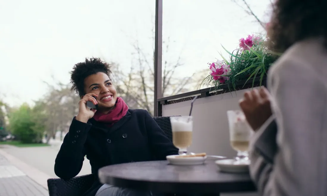 Una mujer sonriendo mientras habla por teléfono en la terraza de un café