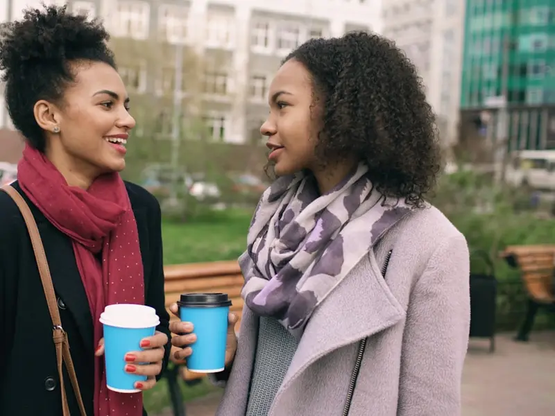 Dos mujeres conversando con un café en la mano, en la calle